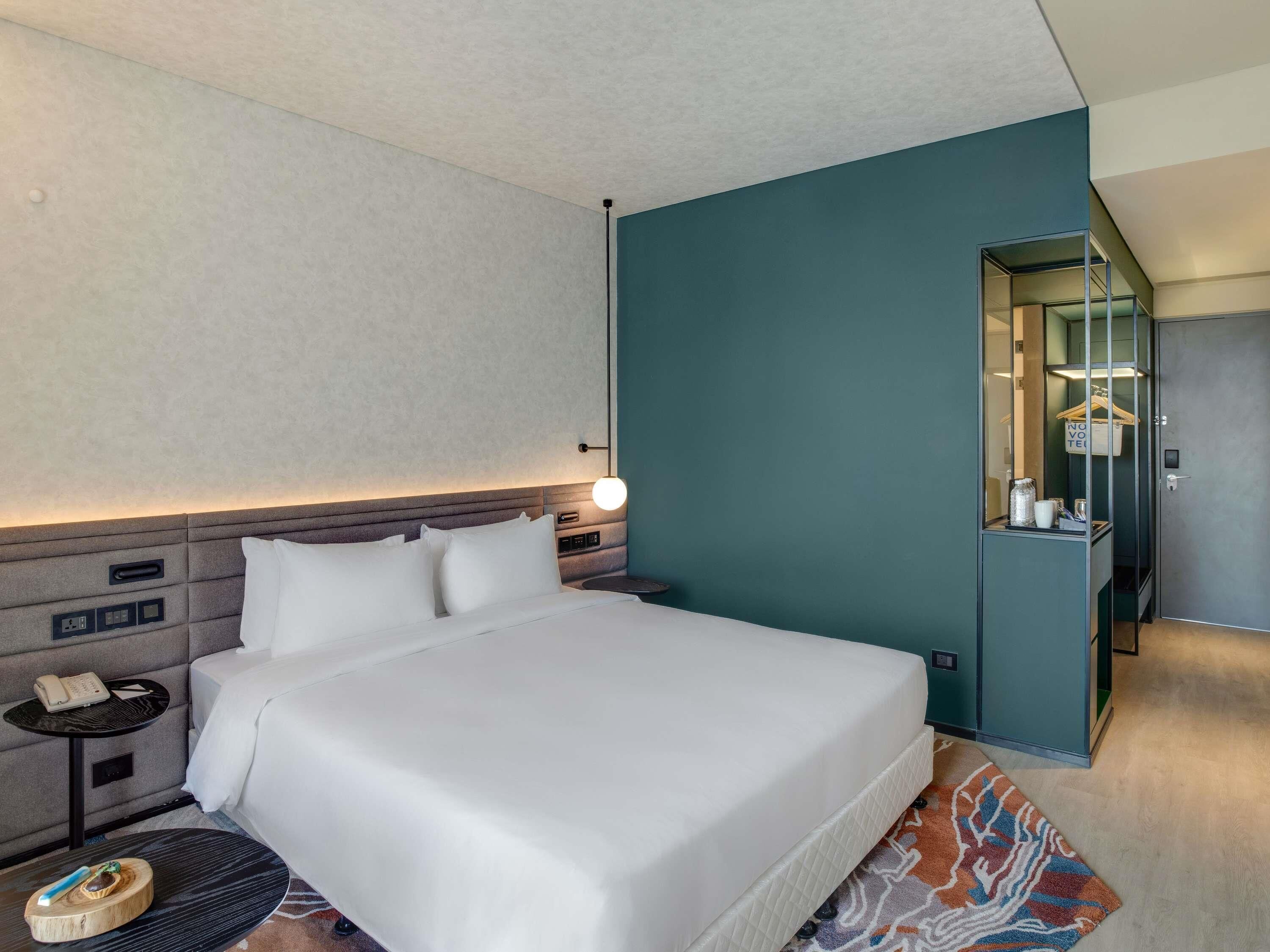 Ein modernes Hotelzimmer mit einem großen Bett, Nachttischen, einem Spiegel und Blick auf den Flur.