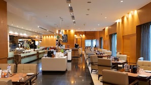 Un moderno vestíbulo de hotel con una zona de buffet, arreglos de asientos y una recepción.