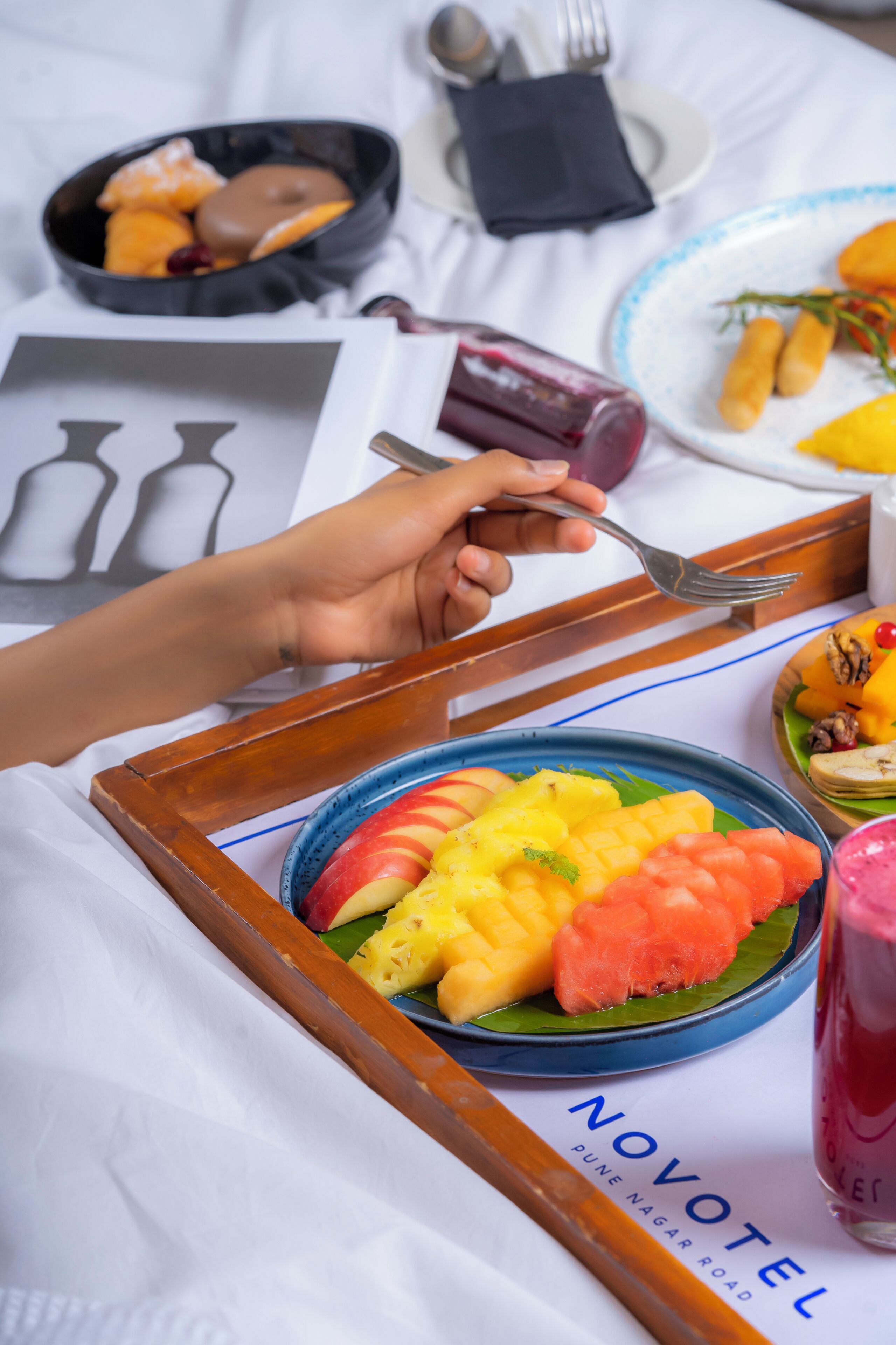 A tray with a plate of fruit and a glass of juice on a bed.