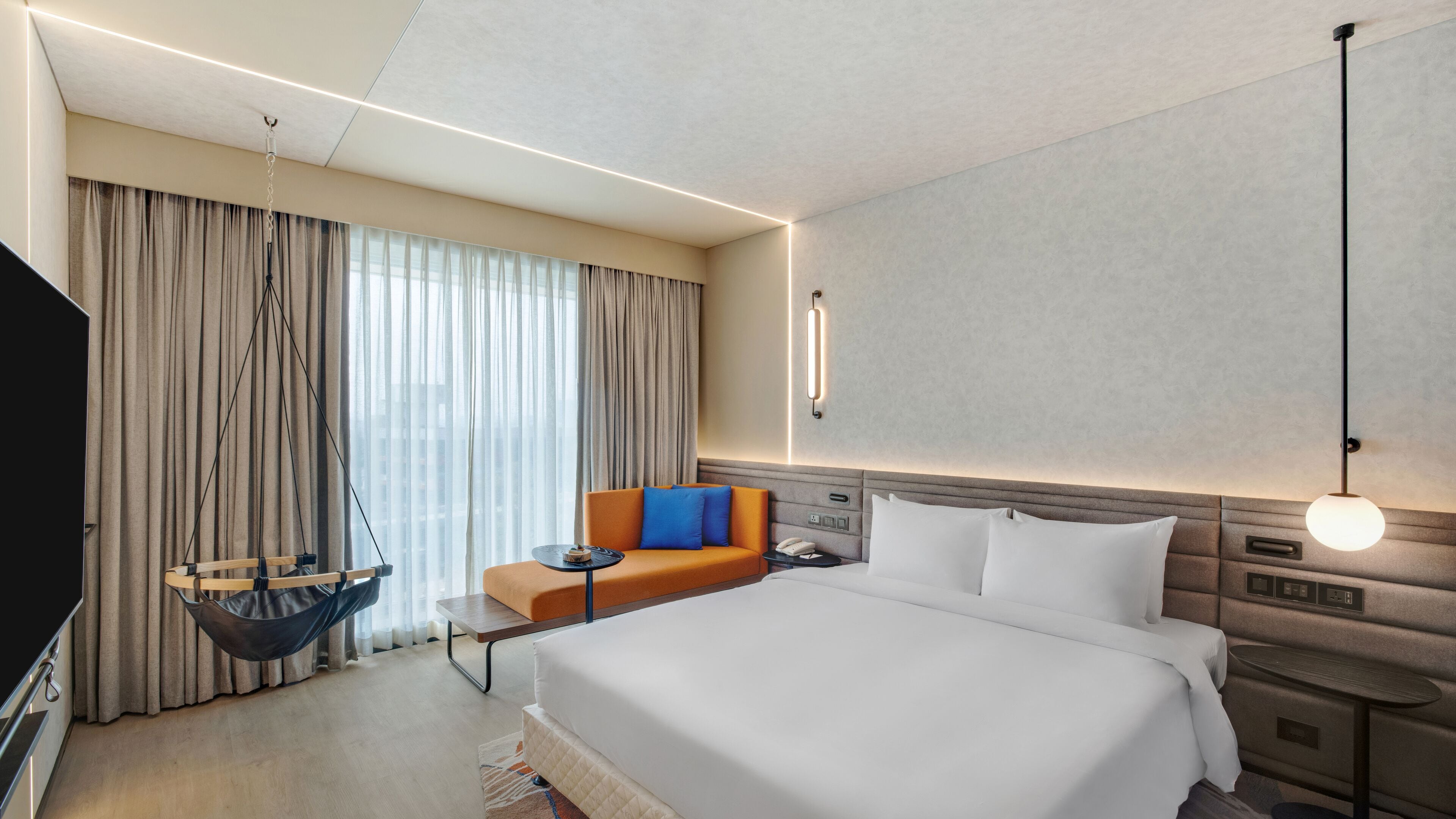 A modern hotel room with a large bed, a sofa, a hanging chair, and a television.