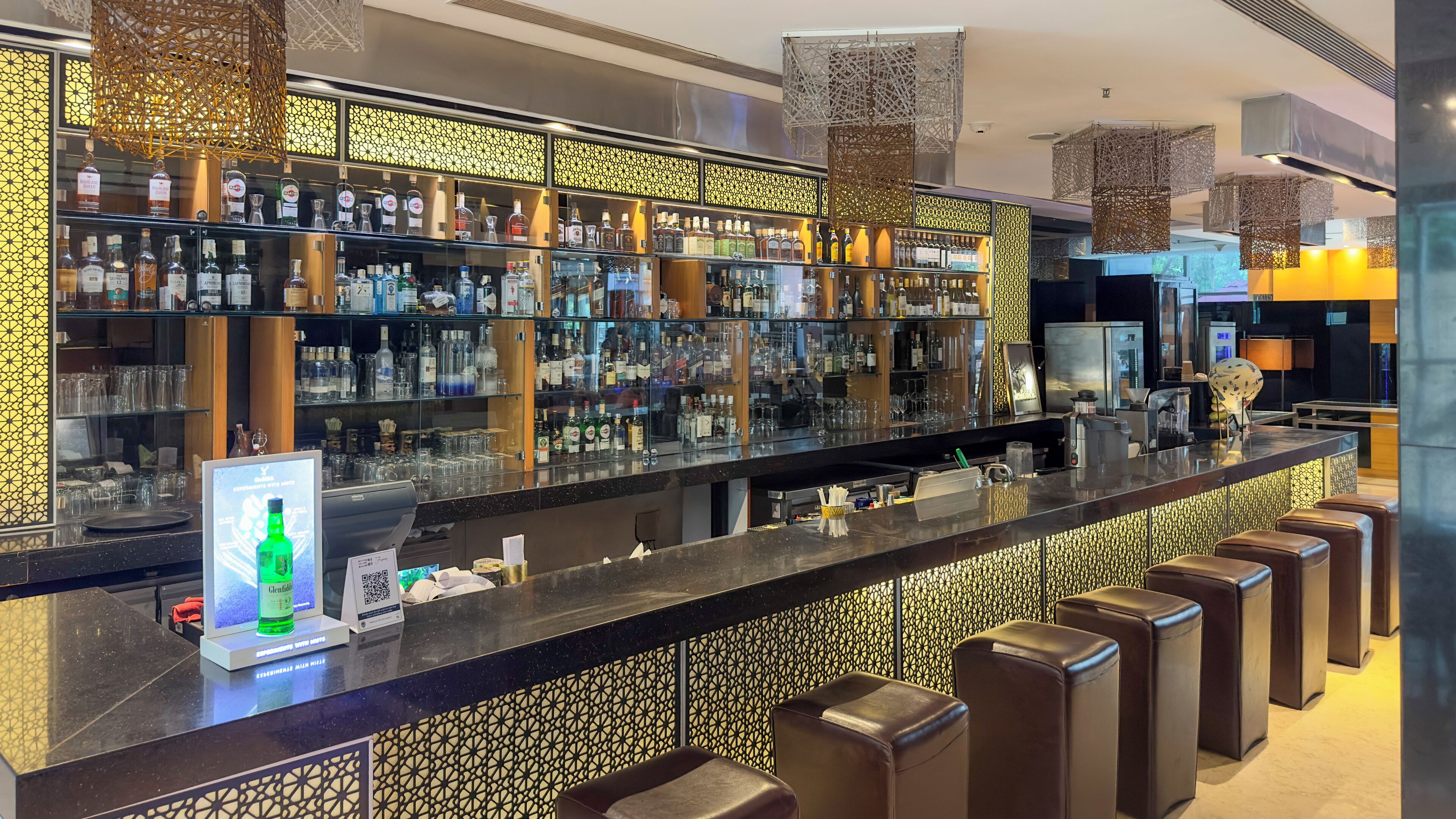 Una zona de bar con una barra larga, estantes llenos de botellas de licor y un código QR para pagos digitales.