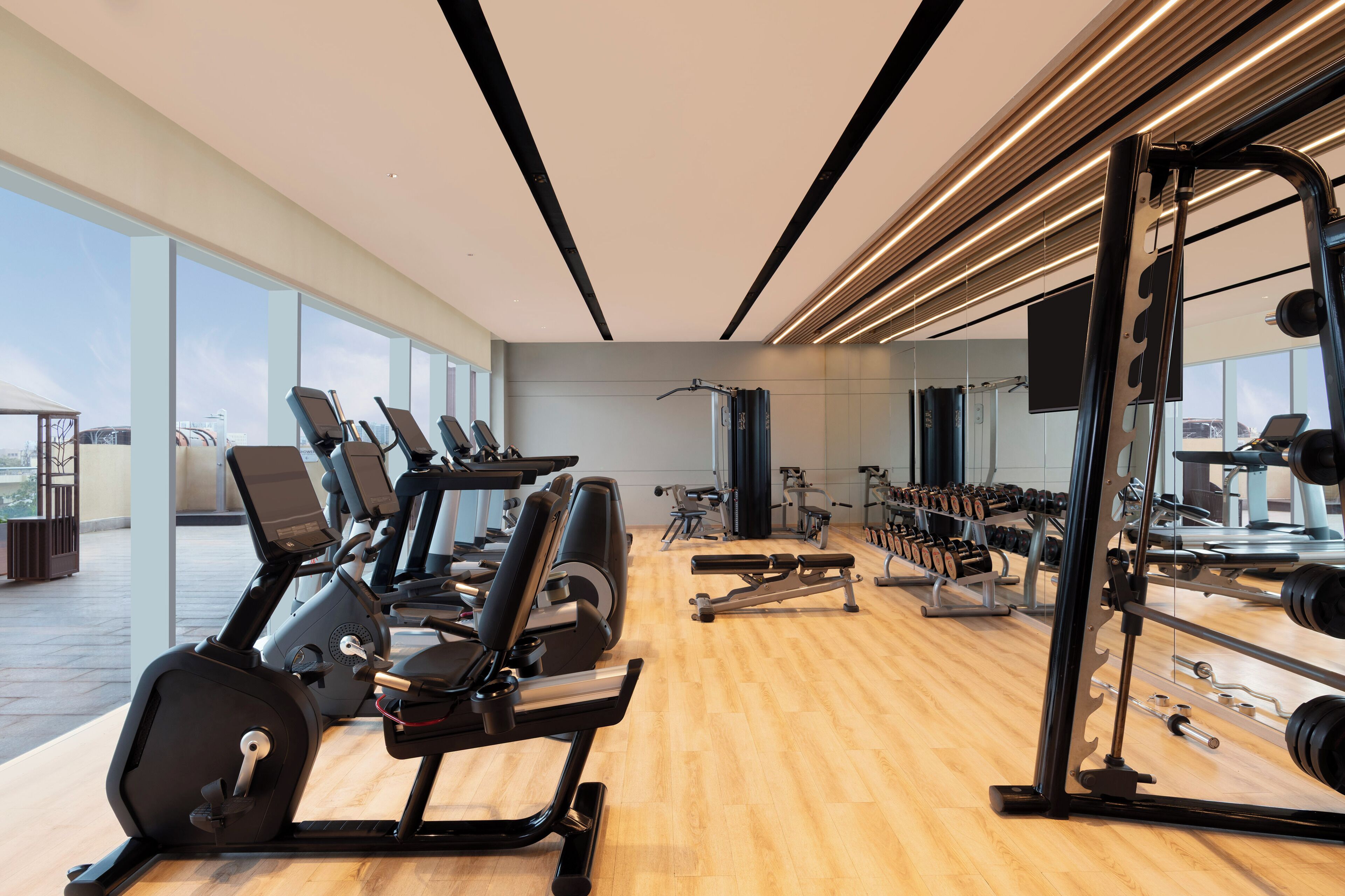 A gym with exercise equipment, large windows, and a wooden floor.