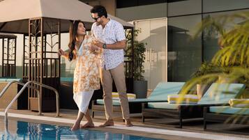 A swimming pool area with lounge chairs, a covered seating area, and a modern building in the background.
