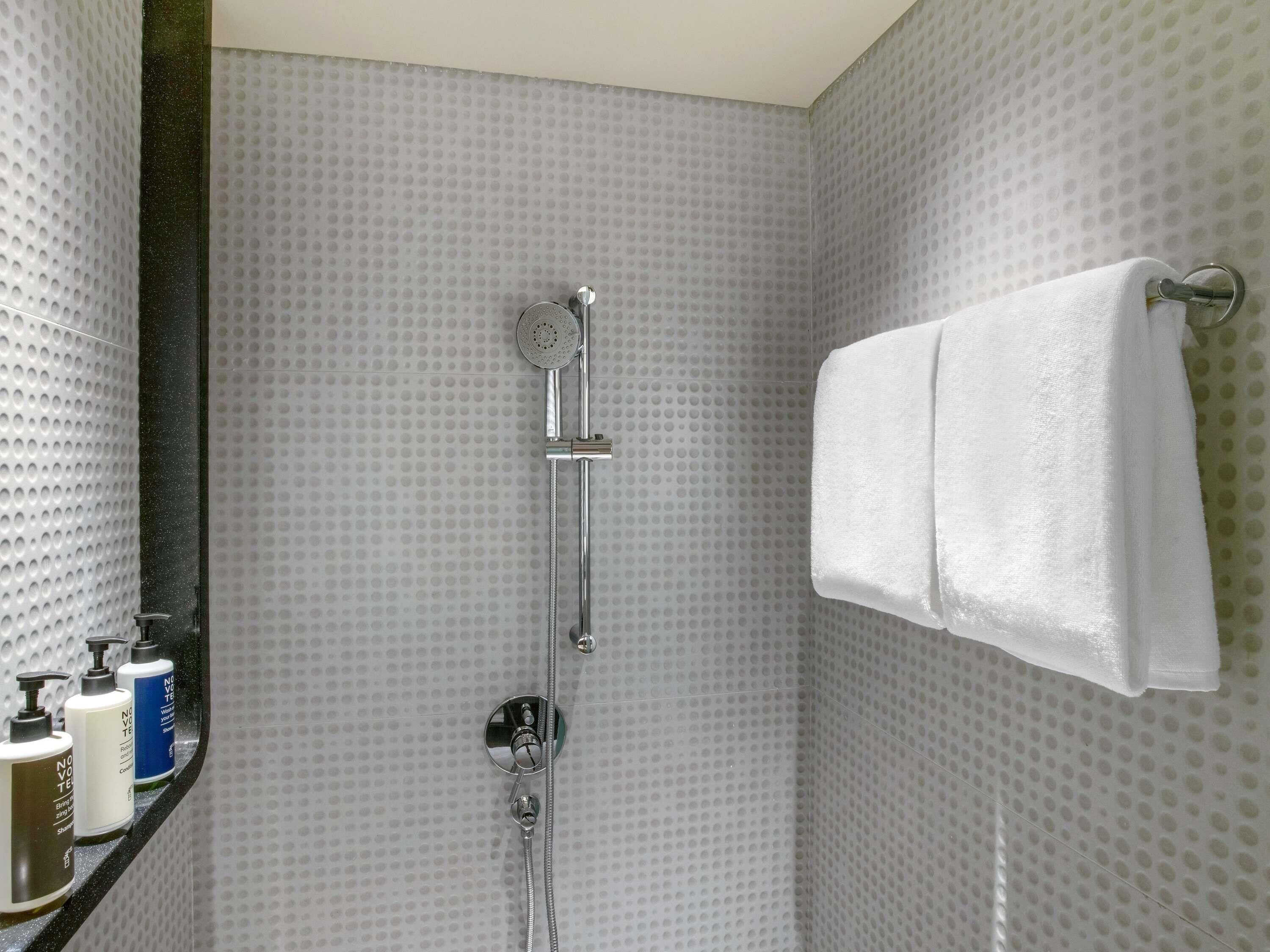 A shower with a handheld showerhead, a towel rack with a white towel, and toiletries on a shelf.