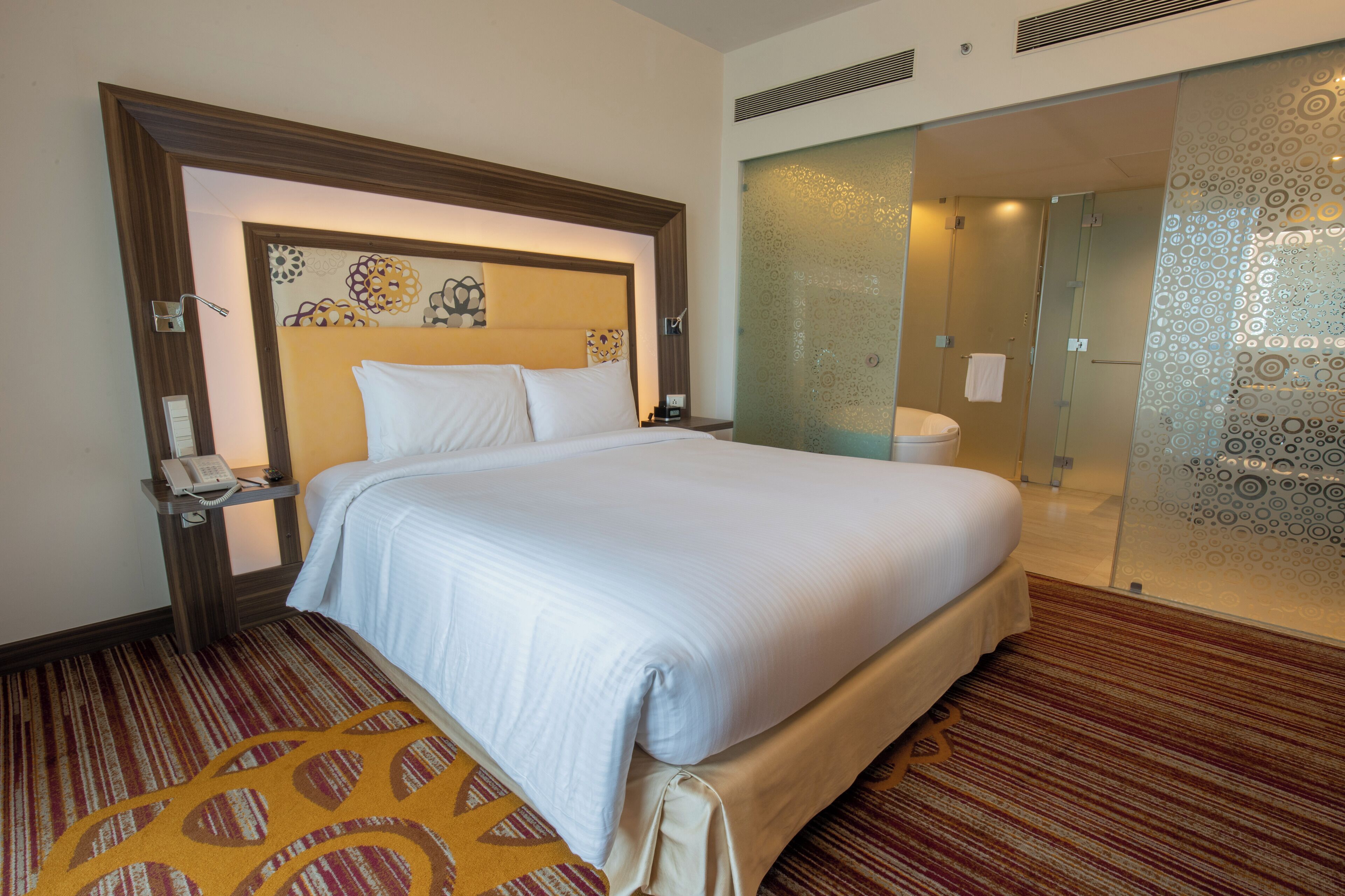 A hotel room with a large bed, a bedside table with a phone, and a glass-enclosed shower area.