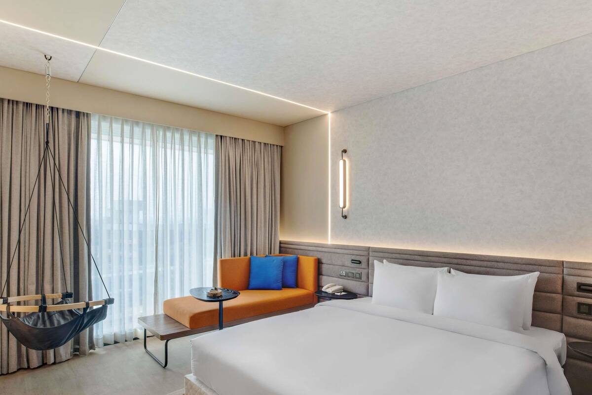A hotel room with a large bed, a sofa, a hanging chair, and a bedside table.