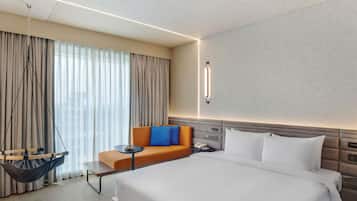 A hotel room with a large bed, a sofa, a hanging chair, and a bedside table.