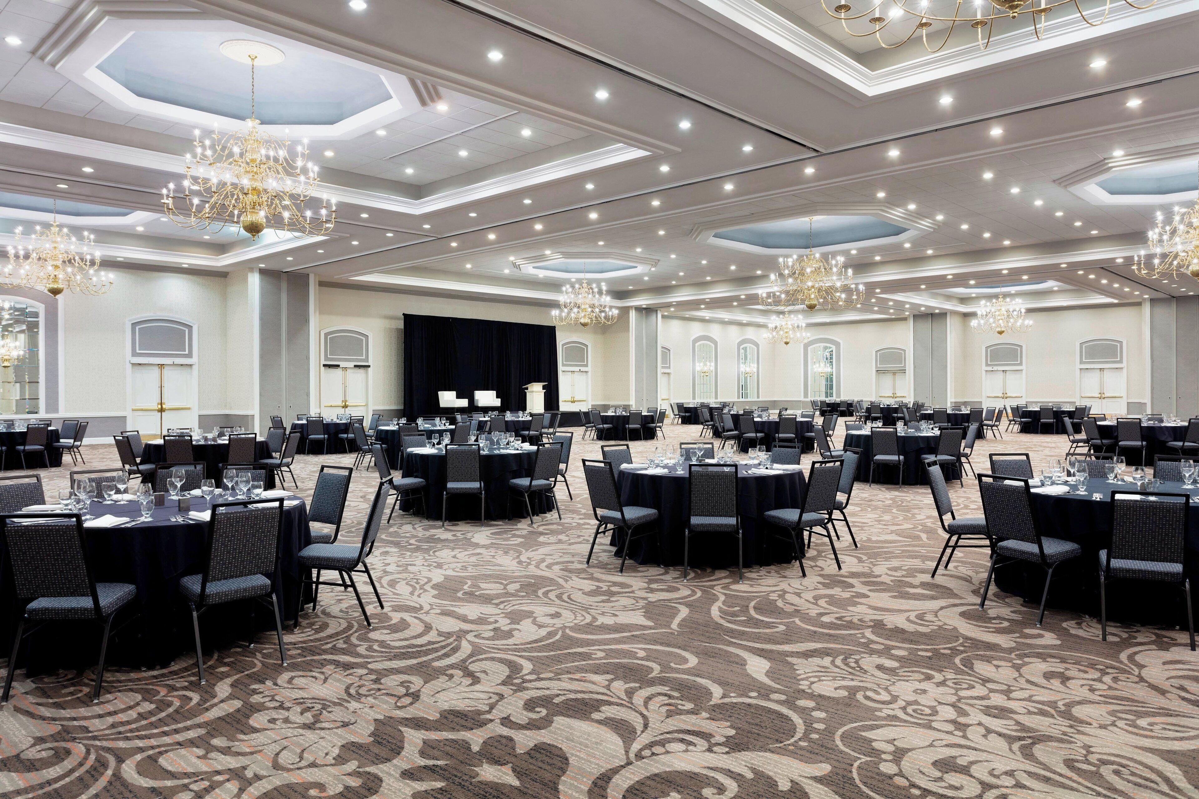 Un amplio salón de banquetes con mesas y sillas redondas, candelabros y una alfombra estampada.