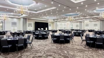 Un amplio salón de banquetes con mesas y sillas redondas, candelabros y una alfombra estampada.