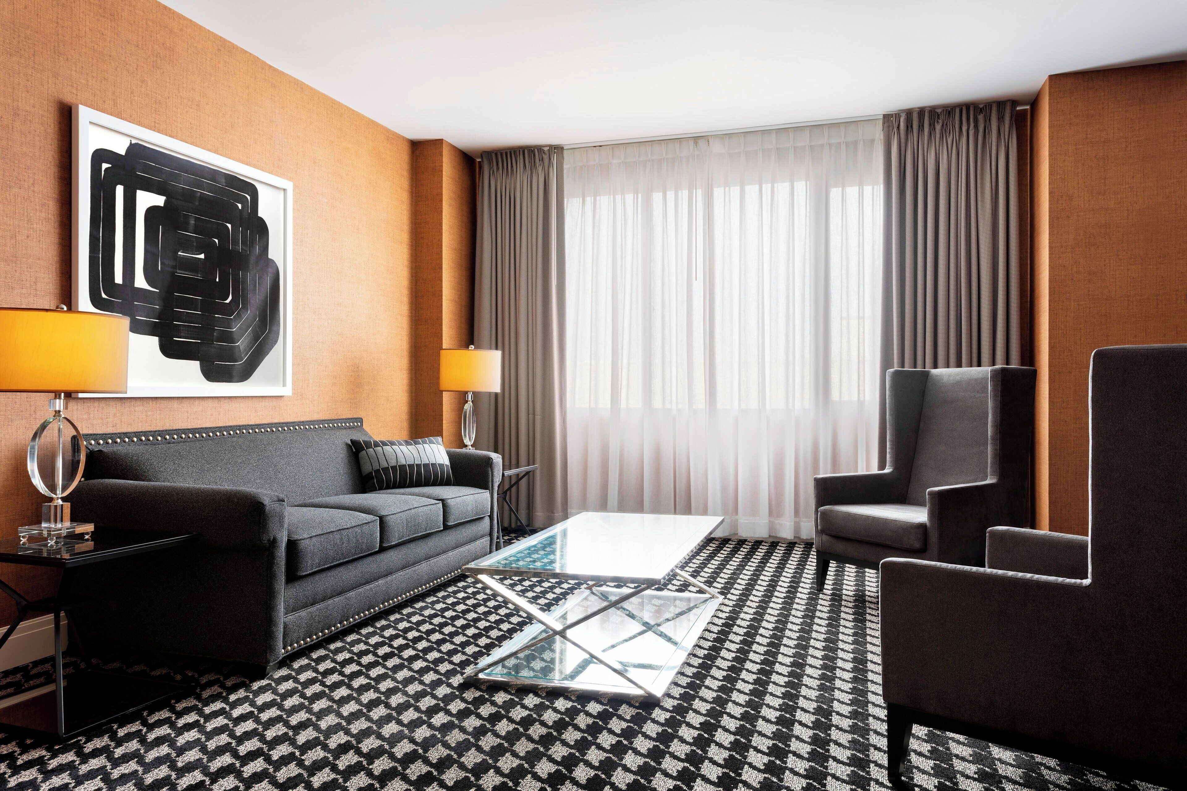 Moderni hotellihuone, jossa on sohva, nojatuoleja, sohvapöytä ja suuri abstrakti taulu seinällä.