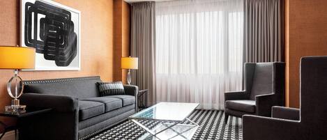 Moderni hotellihuone, jossa on sohva, nojatuoleja, sohvapöytä ja suuri abstrakti taulu seinällä.