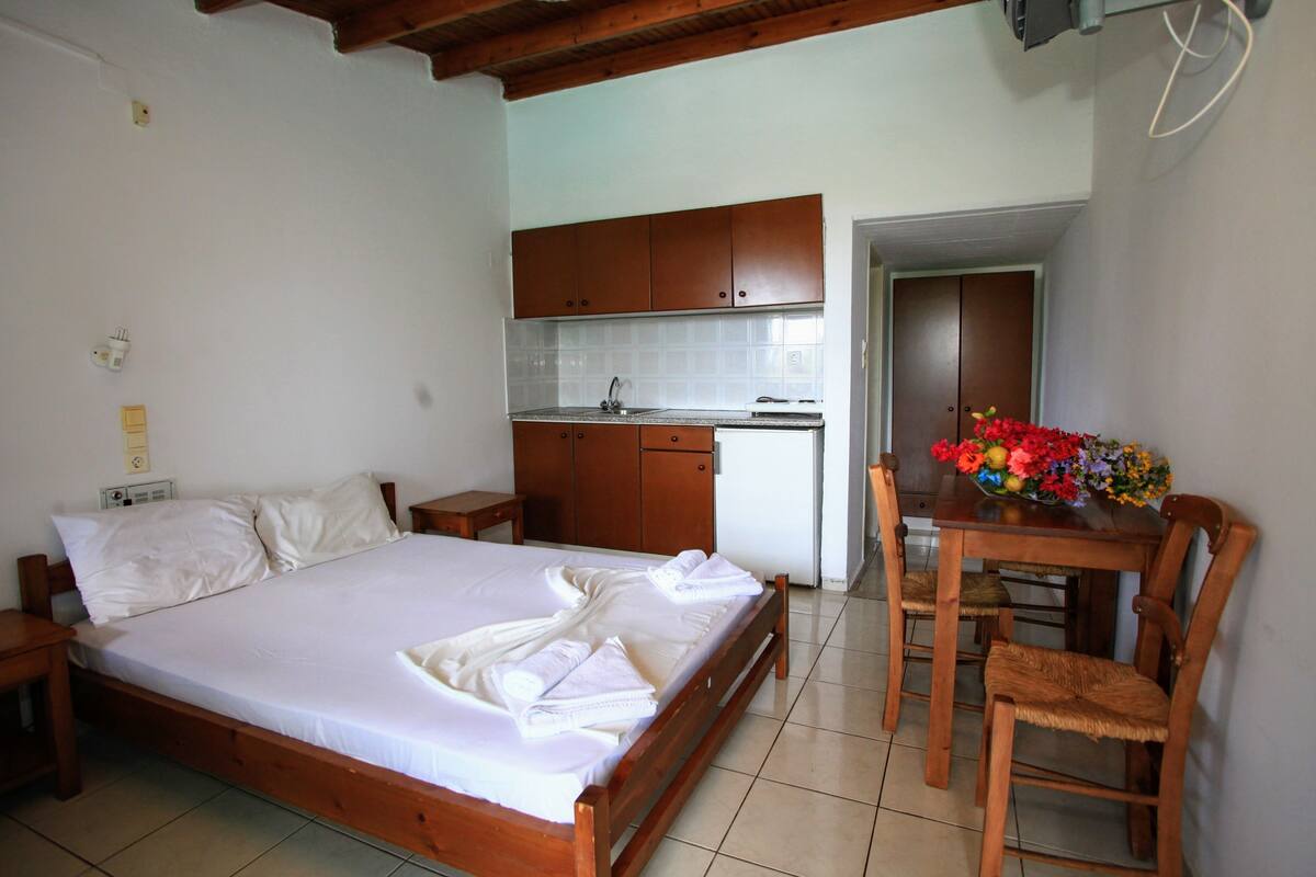 Ein Schlafzimmer mit einem hölzernen Bett, einer kleinen Küchenzeile und einem Essbereich mit Tisch und Stühlen.