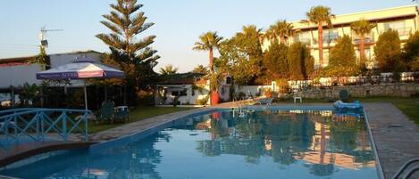 A swimming pool with a stone deck, surrounded by palm trees and a building with balconies.
