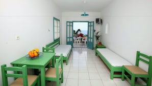 A small, bright room with green furniture, a dining table with fruit, and a view of the sea through an open door. - Anatoli Apartments (Hersonissos)