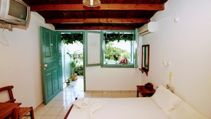 A room with a bed, a wooden ceiling, a TV, and a window with a view of greenery. - Anatoli Apartments (Hersonissos)