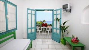 A room with a bed, a small table with chairs, a bench, a TV, and a view of the sea through an open door. - Anatoli Apartments (Hersonissos)