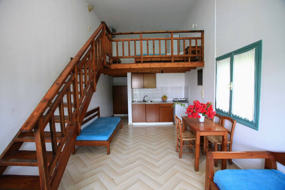 Eine kompakte Küche mit Einbauofen, ein Essbereich mit Holztischen und -stühlen sowie eine Treppe, die in einen oberen Bereich führt.