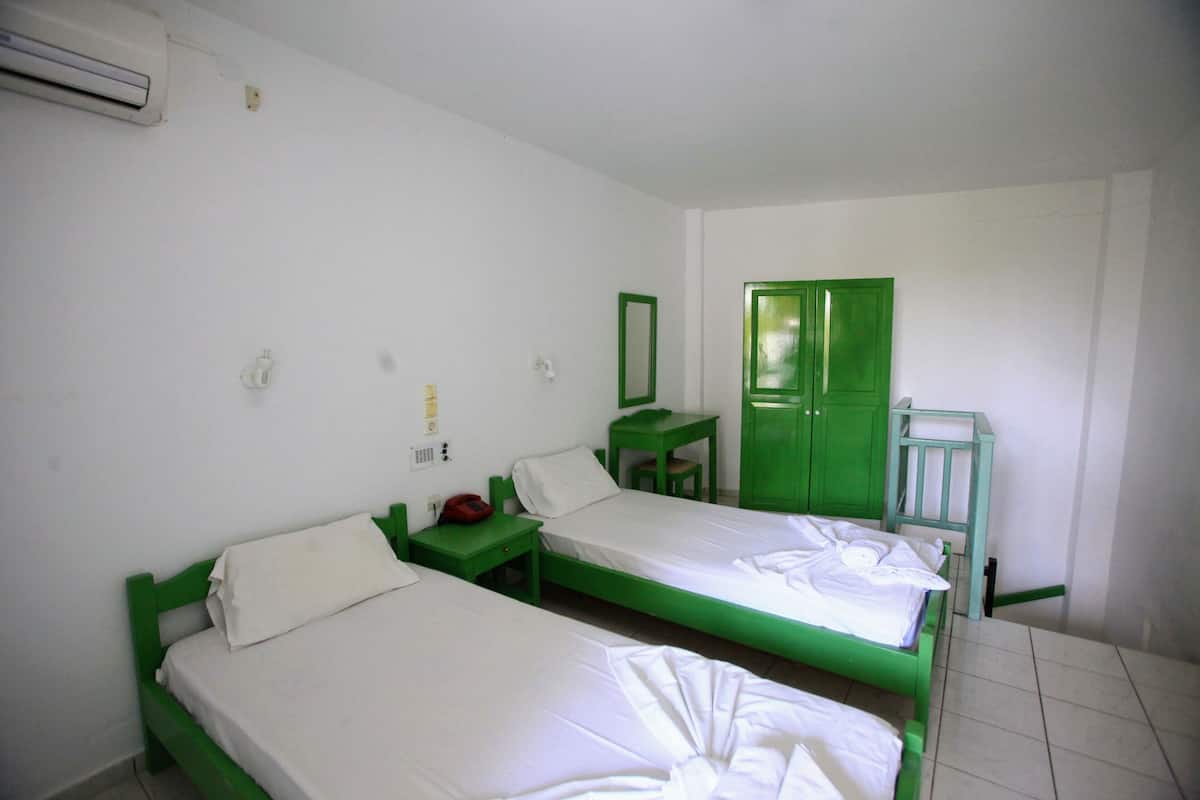 Ein Zimmer mit zwei Einzelbetten, einem grünen Kleiderschrank, einem kleinen Tisch und einem grünen Stuhl.