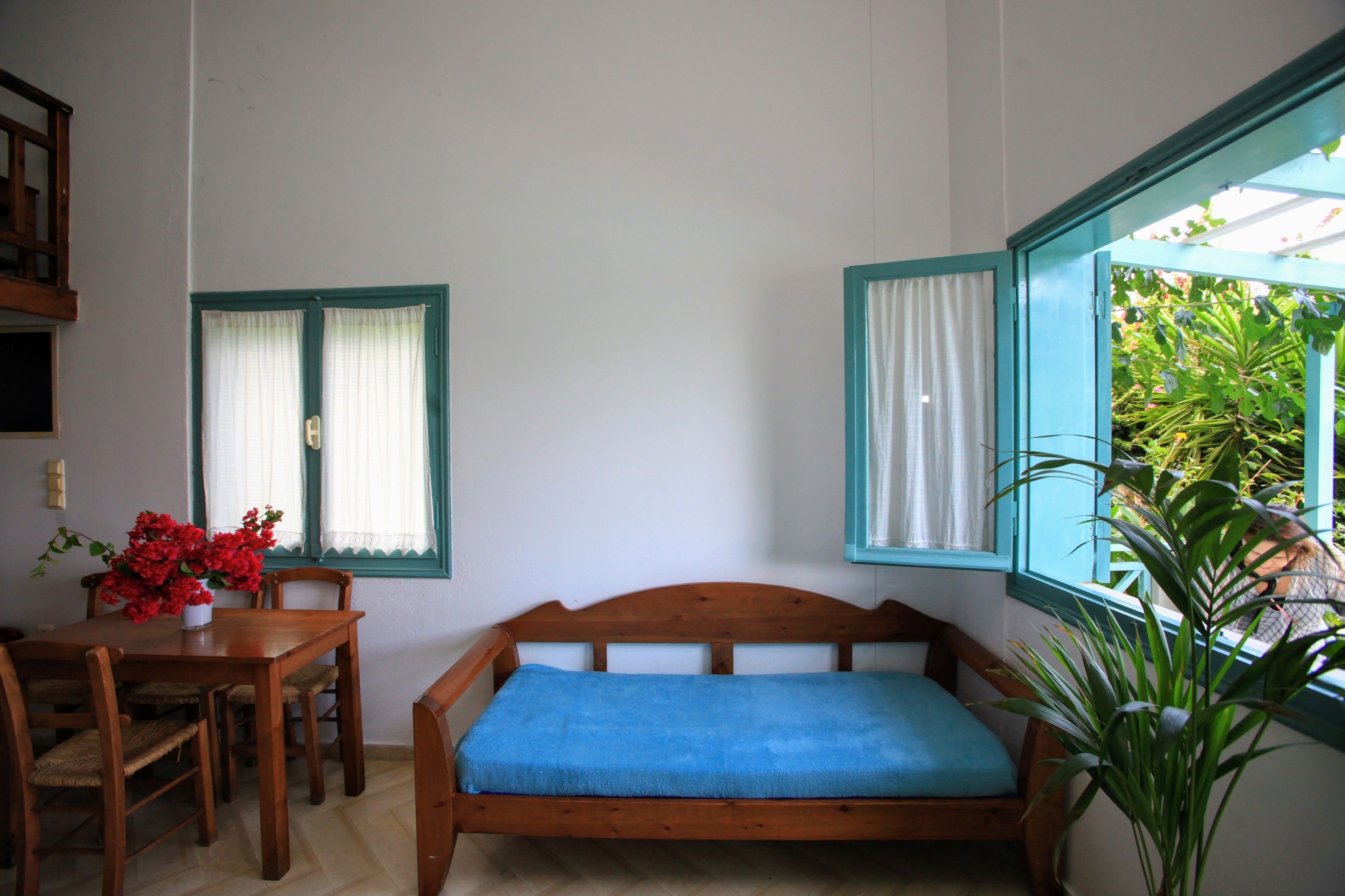 Una habitación con una cama de madera, una mesa de comedor con sillas y dos ventanas con cortinas.