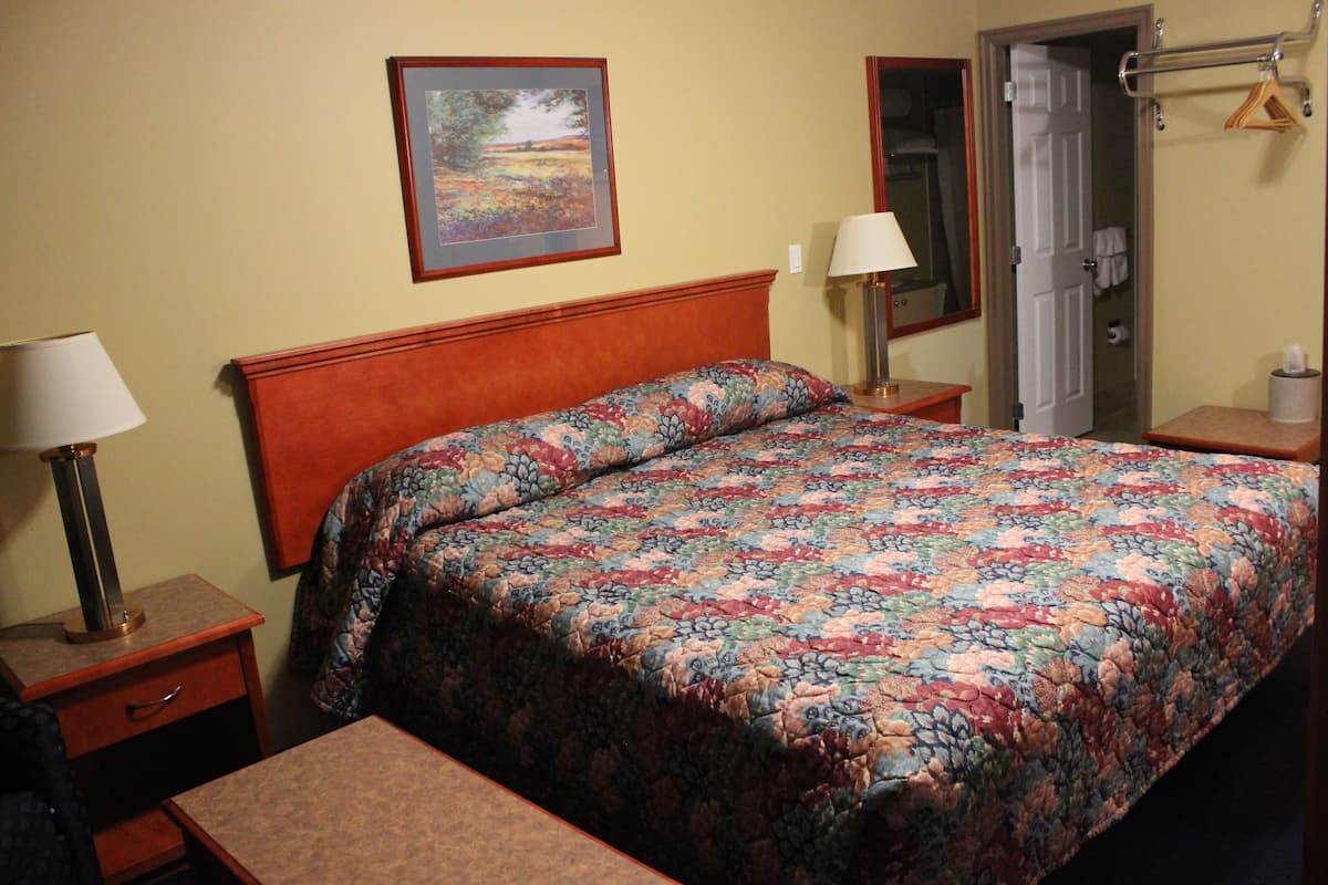 A hotel room with a bed, bedside tables, a lamp, a framed picture on the wall, and a door.