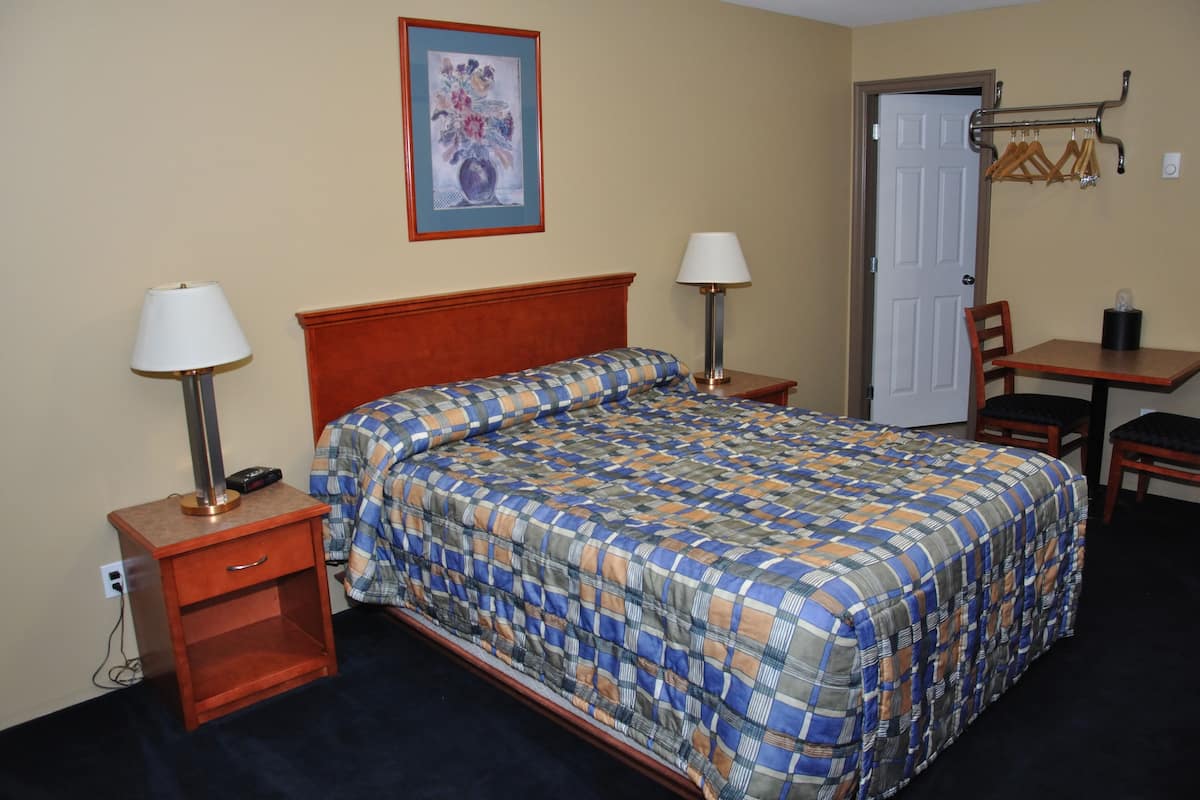 A hotel room with a bed, two bedside tables with lamps, a chair, a small table, and a door.