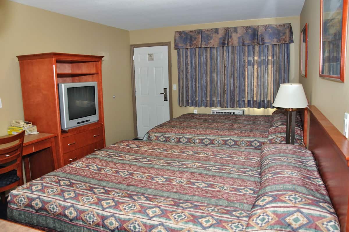 A hotel room with a bed, a desk with a television, a lamp, and a door.