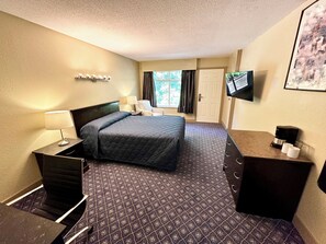 Una habitación de hotel con cama, escritorio con cafetera, televisor y ventana con cortinas.