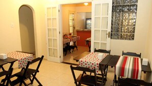 Un espace repas avec des tables et des chaises, une cuisine en arrière-plan et une porte donnant sur une autre pièce.