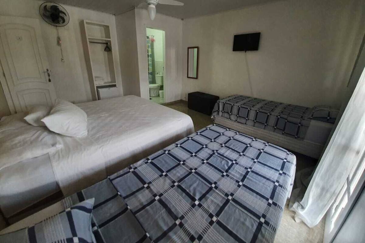A room with two beds, a ceiling fan, a television, and a door leading to a bathroom.