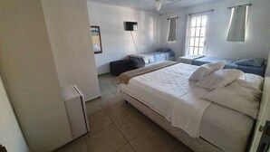 Une chambre avec un lit, un ventilateur de plafond, un petit réfrigérateur et une fenêtre avec des rideaux.