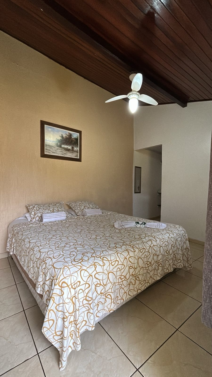 Een slaapkamer met een bed, een plafondventilator, een ingelijst schilderij aan de muur en een deur naar een andere kamer.