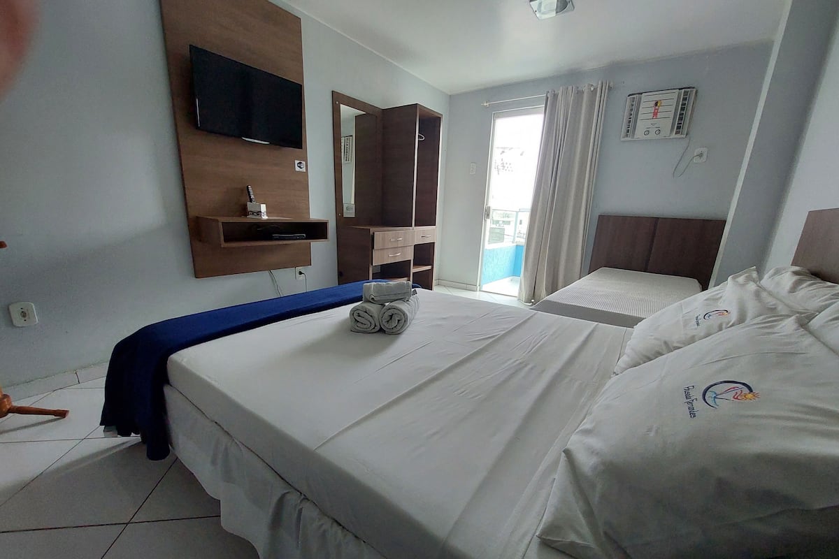 Habitación de hotel con dos camas, televisión montada en la pared, un escritorio pequeño y una ventana con cortinas.