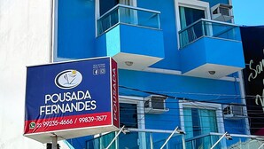 A blue building with balconies and a sign for 'Pousada Fernandes' with contact numbers. - Pousada Fernandes (Arraial do Cabo)