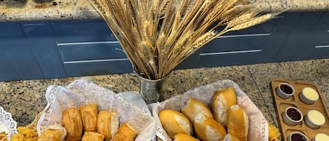 A kitchen counter with two baskets of bread, a metal container with wheat stalks, and a tray with jam and butter.