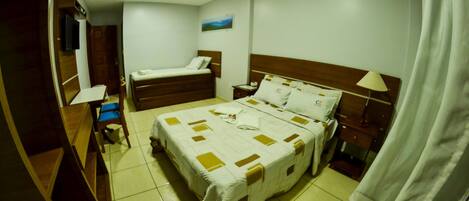 Una habitación de hotel con una cama grande, una cama más pequeña, un escritorio, una silla, un televisor y un ventilador de techo.