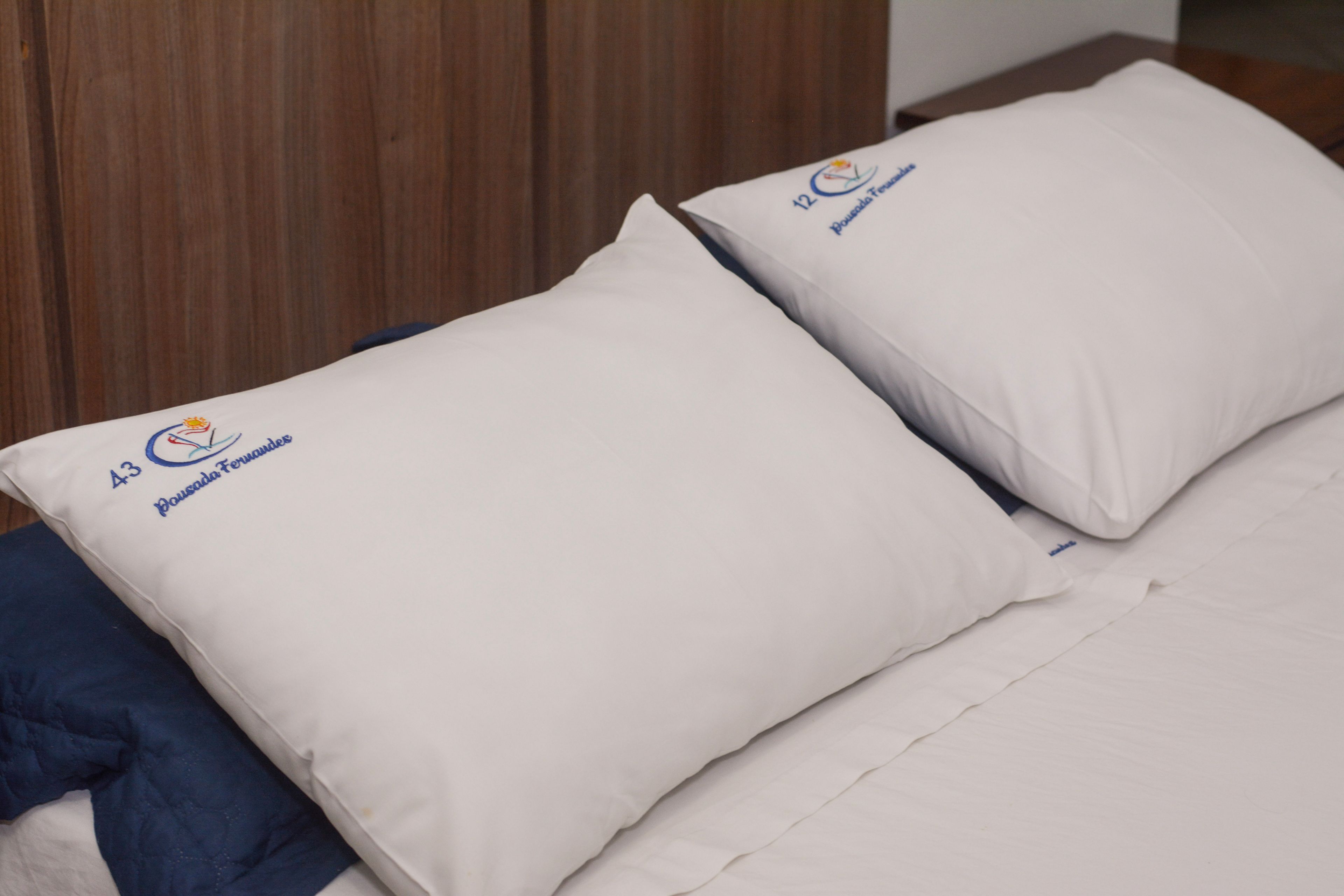 Two pillows with embroidered text and a bed with a blue blanket.
