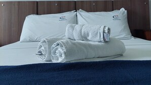 A neatly made bed with white linens and a rolled towel, two framed pictures on the wall, and a wooden headboard. - Pousada Fernandes (Arraial do Cabo)