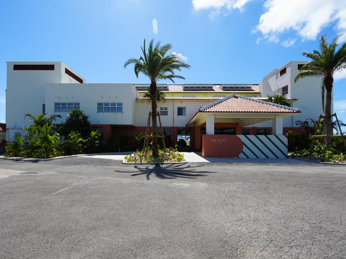 A hotel with a modern design, featuring a flat roof, a central entrance, and a parking lot.