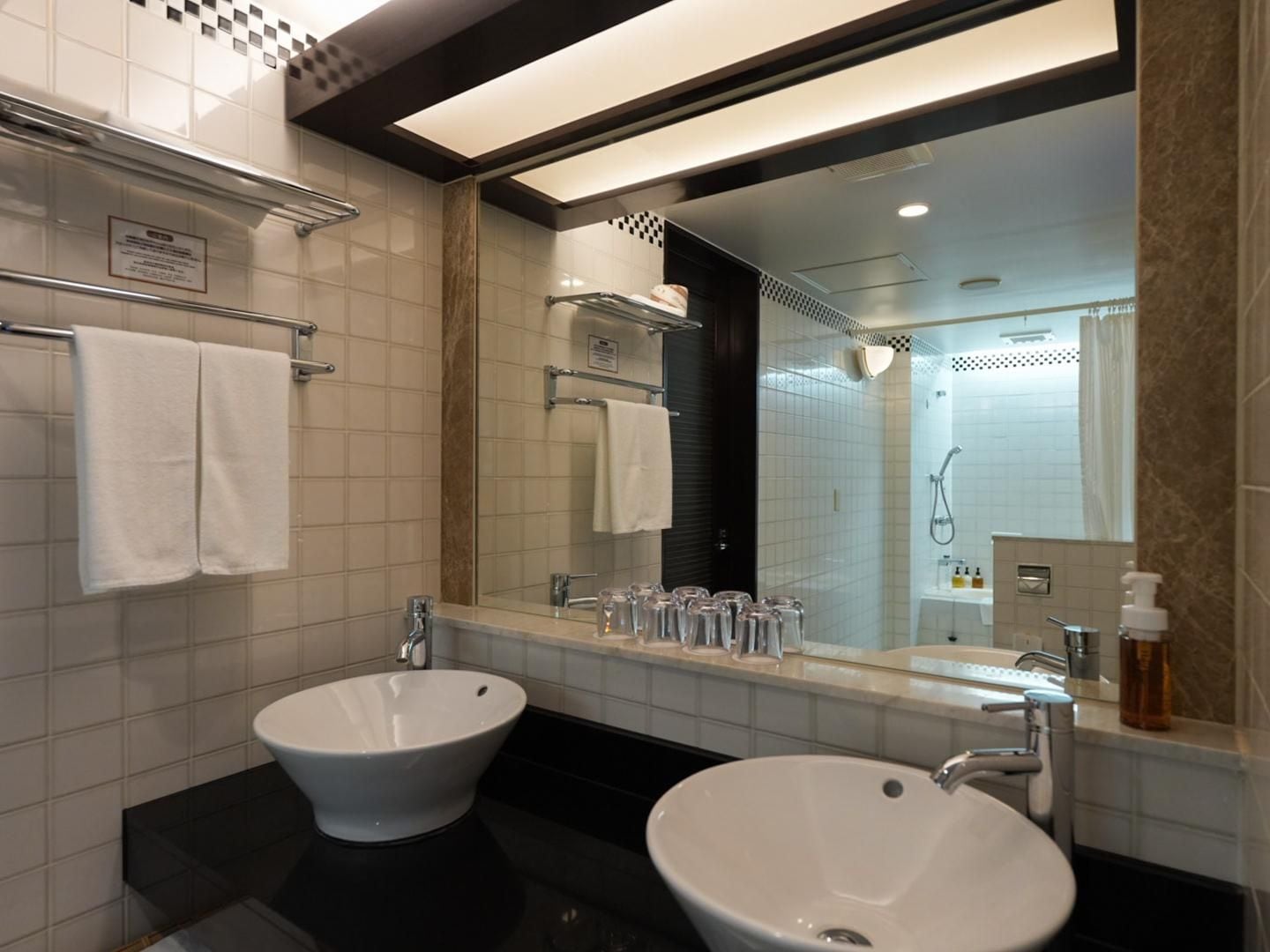 A modern bathroom with two sinks, a large mirror, and a shower area.