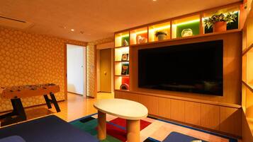 Una habitación con una televisión de pantalla grande, una mesa de futbolín y una alfombra colorida.