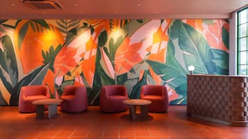 Un vestíbulo con un gran mural tropical, asientos rojos y un mostrador de recepción.