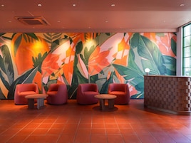 Un vestíbulo con un gran mural tropical, asientos rojos y un mostrador de recepción.