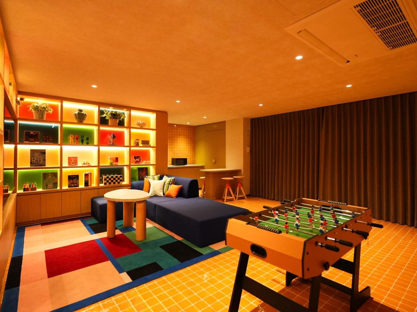 A room with a foosball table, a sofa, a small round table, and a wall with shelves containing various items.