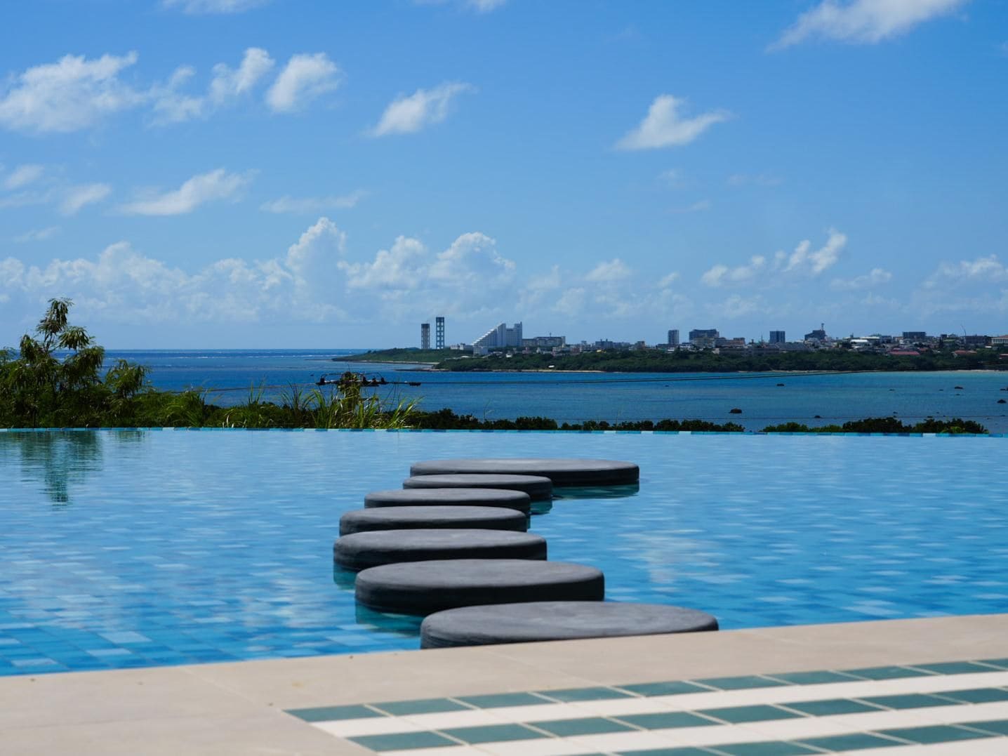 A swimming pool with a clear view of a distant city skyline and ocean.