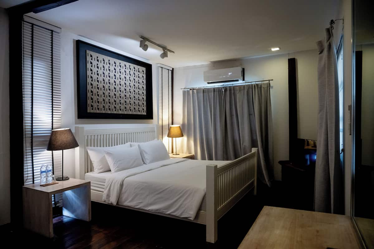 Een hotelkamer met een bed, nachtkastjes, een lamp, een radiator en een raam met zonwering.