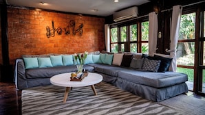 A modern living room with a large sectional sofa, a round coffee table, and a brick wall with a decorative metal sign.
