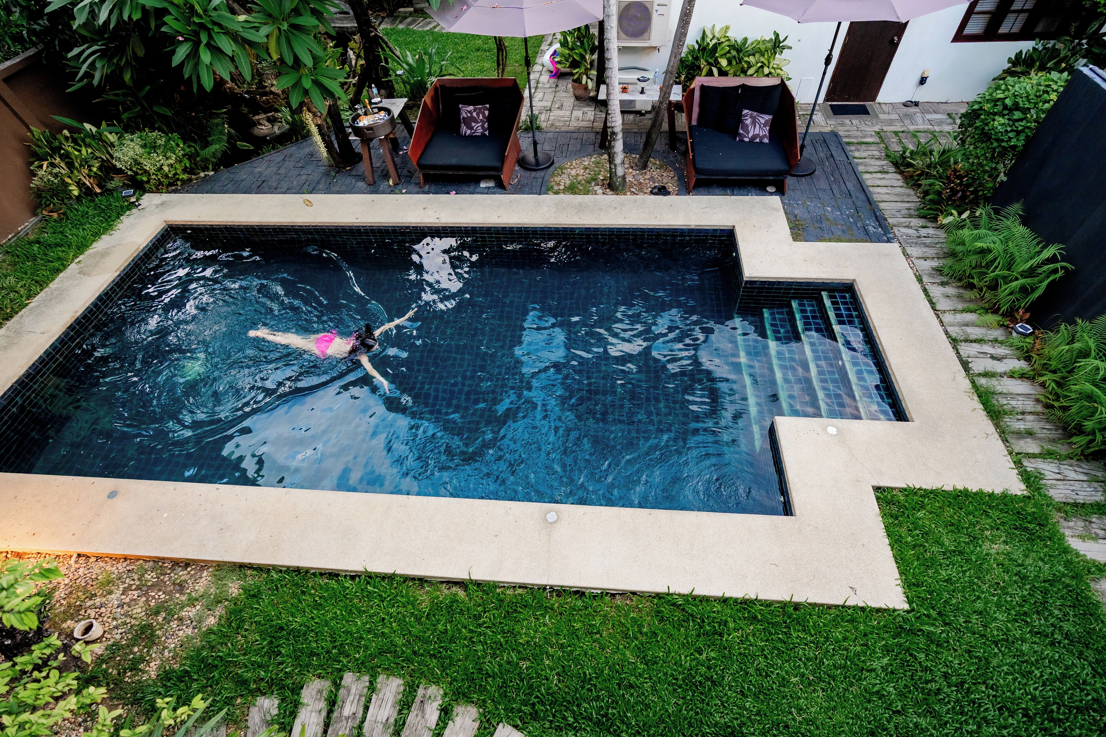 Una piscina rectangular con bordeado de azulejos, rodeada de césped y algunas sillas de descanso.