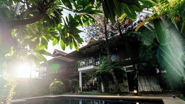 A pool surrounded by lush greenery and a two-story building with a balcony.