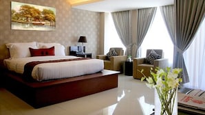 A modern hotel room with a large bed, a desk, a chair, and a view of the outdoors through the window.