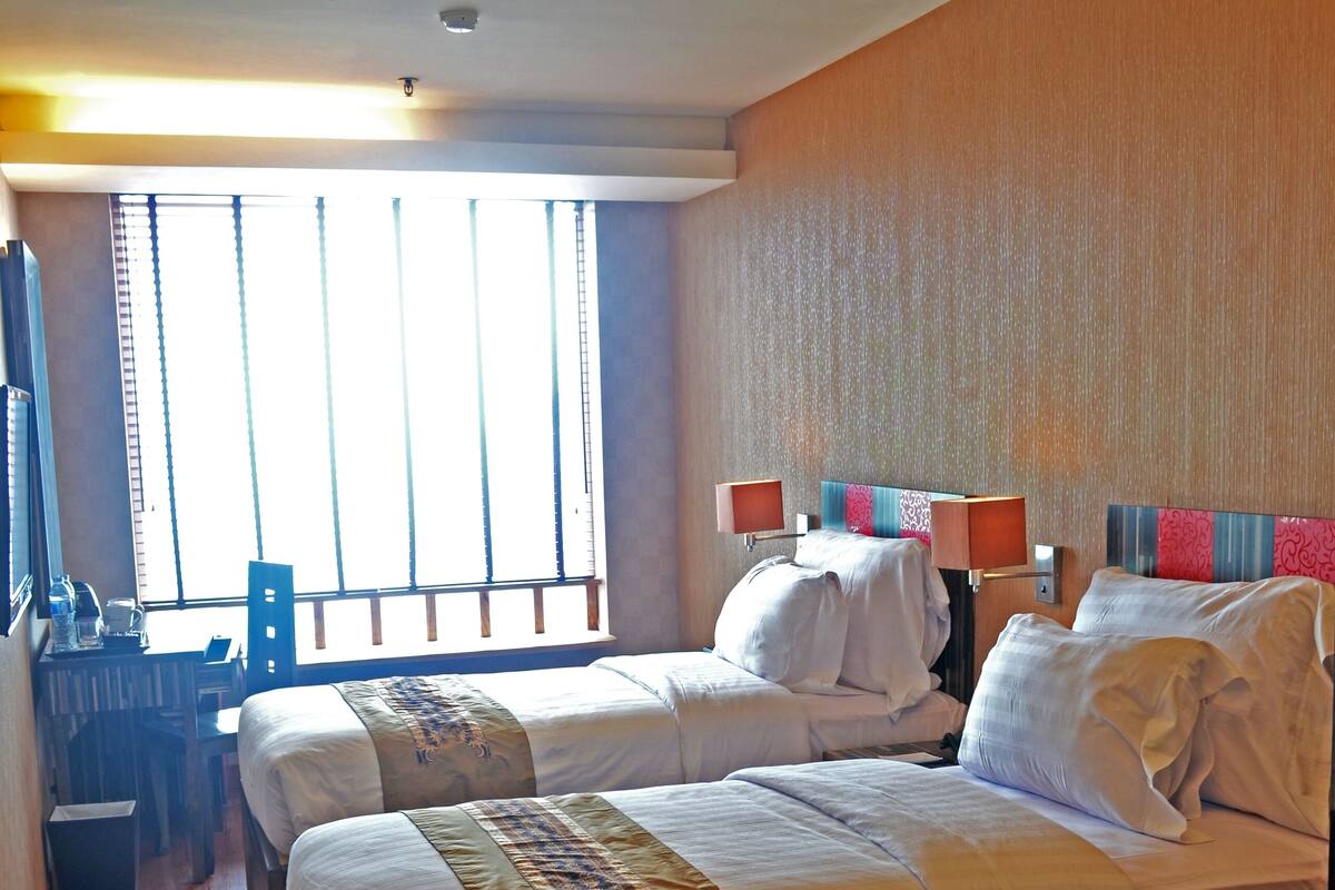 A hotel room with two beds, a desk, and a large window.